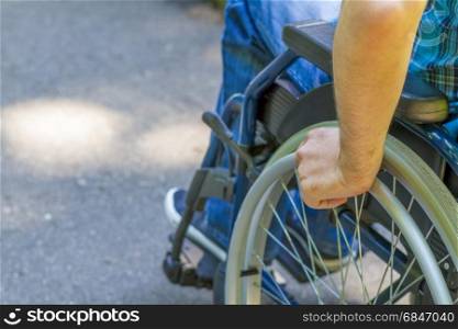 hand of young man on the wheel of wheelchair in the city park. hand of young man on the wheel of wheelchair