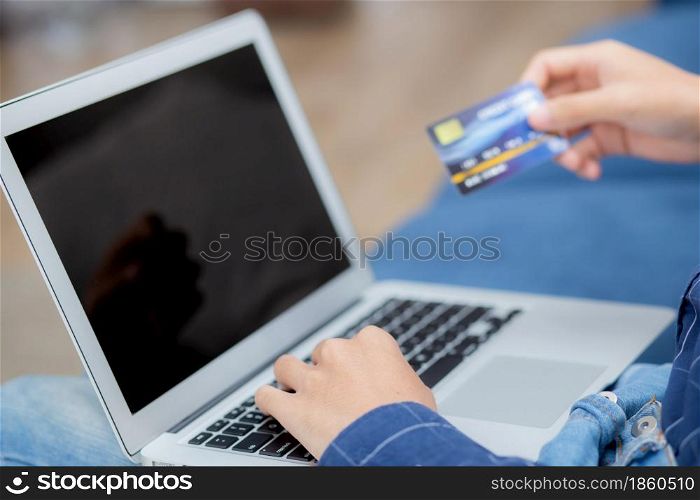 Hand of young man using laptop computer display blank screen shopping online with credit card on sofa at home, male purchase and payment with debit card, e-commerce and technology, lifestyle concept.