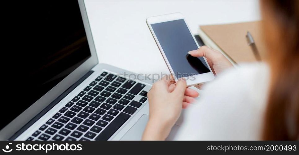 Hand of young woman working with laptop computer and smartphone mockup on desk at home, notebook and phone display blank screen, freelance look message to internet, business and communication concept.