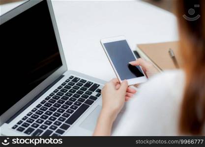Hand of young woman working with laptop computer and smartphone mockup on desk at home, notebook and phone display blank screen, freelance look message to internet, business and communication concept.