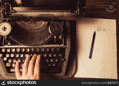 hand on a typewriter on a wooden background and a white sheet and ballpoint pen. Retro style.. hand on a typewriter on a wooden background and a white sheet and ballpoint pen. Retro style
