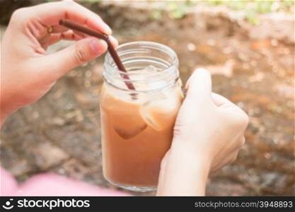 Hand on glass of iced milk coffee with vintage filter effect, stock photo