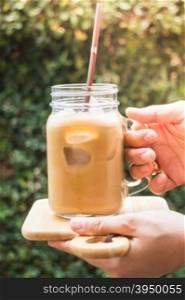 Hand on glass of iced milk coffee with vintage filter effect, stock photo