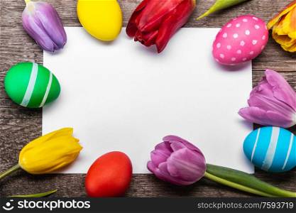 Hand-painted easter eggs with tulips on blank greeting card over wooden background copy space for text. Easter egg and tulips on wood