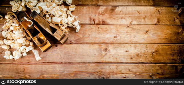 Hand planer with wooden sawdust. On a wooden background. High quality photo. Hand planer with wooden sawdust.