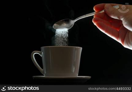hand pouring brown sugar in white cup of coffee