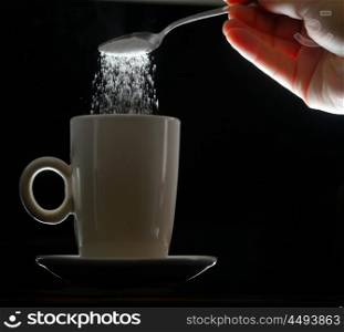 hand pouring brown sugar in white cup of coffee