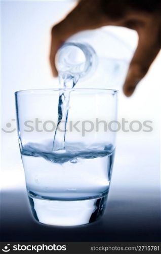 Hand pouring water from a bottle to a half filled glass