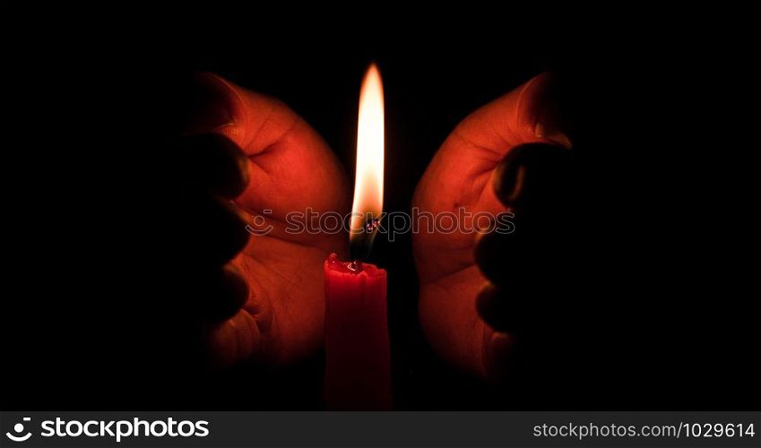 Hand protecting candle light from the wind in darkness on black background