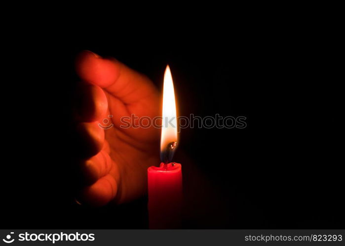 Hand protecting candle light from the wind in darkness on black background