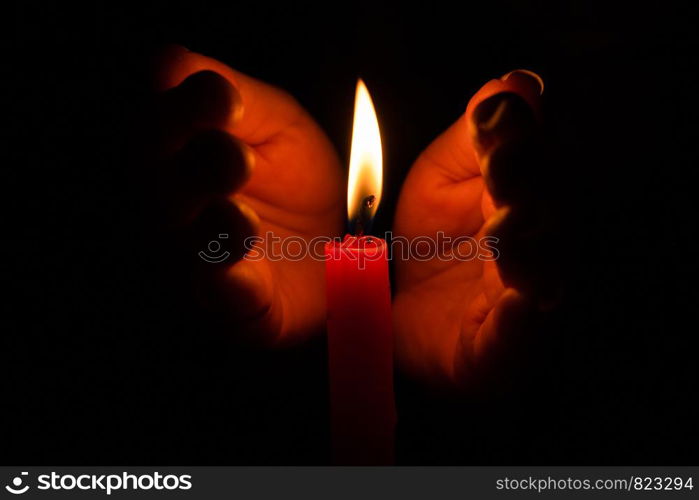 Hand protecting candle light from the wind in darkness on black background