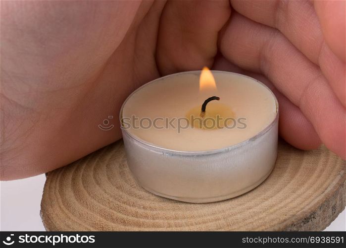 Hand protecting the burning candle placed on piece of wood