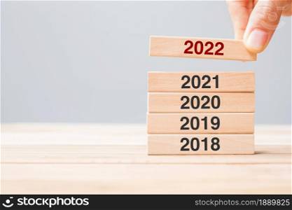 hand pulling 2022 block over 2021, 2020 and 2019 wooden building on table background. Business planning, Risk Management, Resolution, strategy, solution, goal, New Year and happy holiday concepts