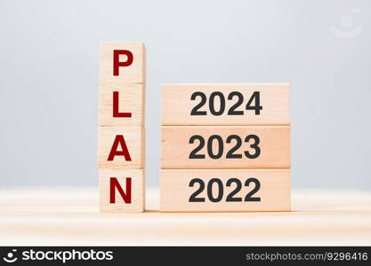 hand pulling 2024 block over 2023 and 2022 wooden building on table background. Business planning, Risk Management, Resolution, strategy, solution, goal, New Year New You and happy holiday concepts