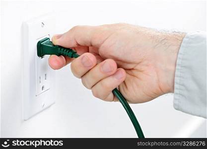 Hand pulling green electrical plug from outlet