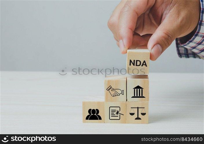 Hand put wooden cubes with Non disclosure Agreement NDA on table and copy space.Business concepts.