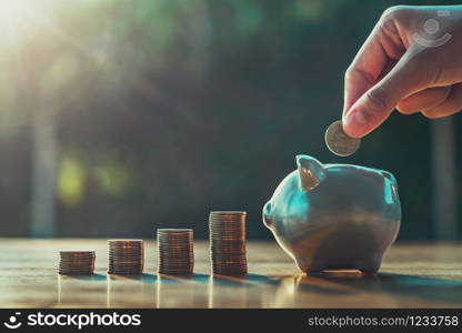 hand puting coins in piggy bank with money stack on desk