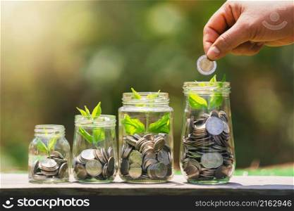 hand putting coins into jug glass with plant growing on money. concept saving finance and accounting