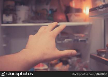 Hand reaching for food in an open fridge