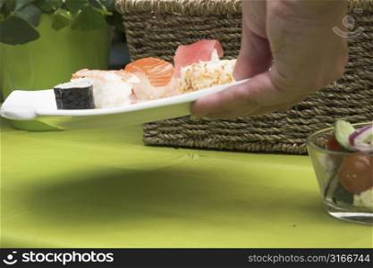 Hand reaching to the table to add a plate of sushi for the picknick lunch for that afternoon (shallow dof)