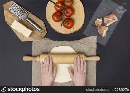 hand rolling pizza dough parchment paper with pizza ingredient black background