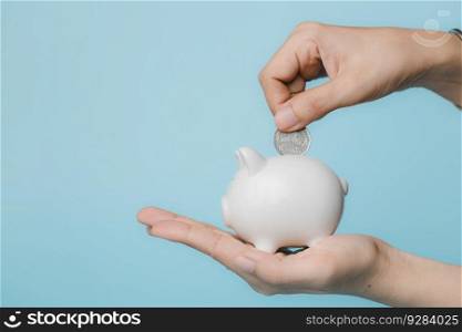 Hand saving a coin into piggy bank  on blue background for investment, business, finance and saving money concept.