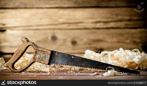Hand saw with wooden shavings. On a wooden background. High quality photo. Hand saw with wooden shavings.
