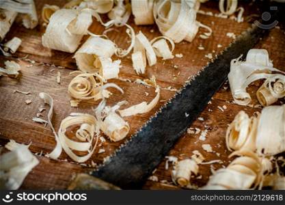 Hand saw with wooden shavings. On a wooden background. High quality photo. Hand saw with wooden shavings.