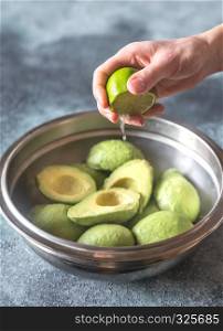 Hand squeezing lime on halved avocados