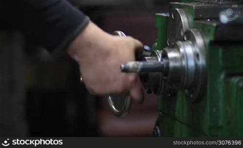 Hand steering adjustable wheel on vintage lathe machine during preparing of cutting metal process in workshop.