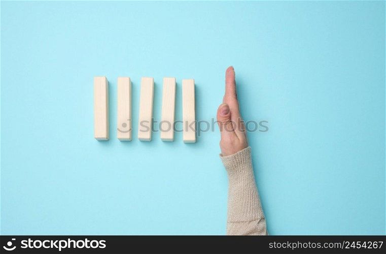 hand stops the fall of wooden blocks on a blue background. Concept of a strong and courageous personality capable of withstanding unequal difficulties. Strong business, control of the situation
