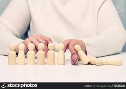 hand stops the fall of wooden figurines of men on a white background. Concept of a strong and courageous personality capable of withstanding unequal difficulties. Strong business