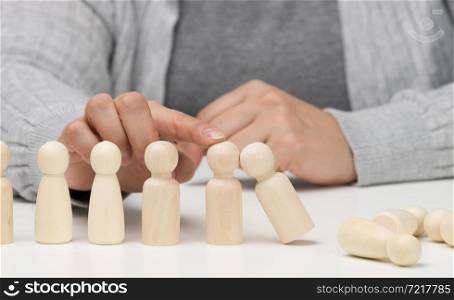hand stops the fall of wooden figurines of men on a white background. Concept of a strong and courageous personality capable of withstanding unequal difficulties. Strong business,