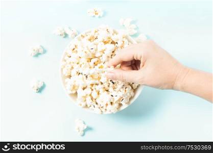 Hand taking popcorn bowl with popcorn over plain blue background. Scattered popcorn over yellow background