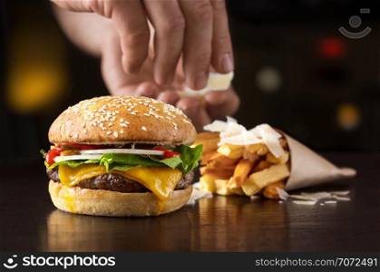 Hand that arranges beef burger with fried potatoes and cheese
