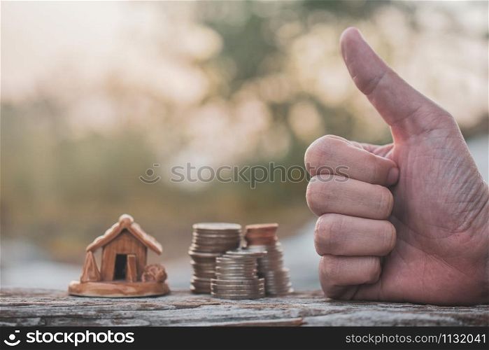 Hand Thump up success with coins stack home model on wood table sunlight background