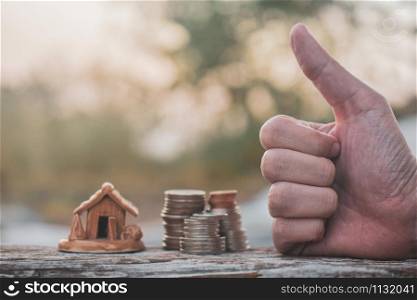 Hand Thump up success with coins stack home model on wood table sunlight background