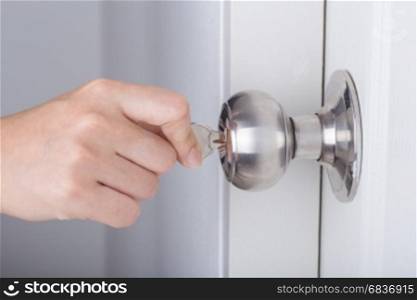 Hand use the key for unlocking door knob on the white door