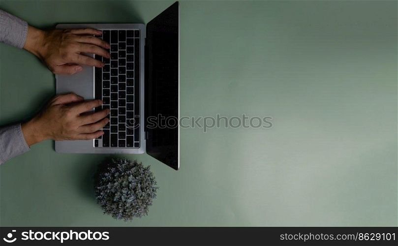 hand using computer laptop and flower on green background.Top view copy space blank.