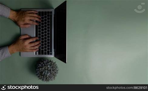 hand using computer laptop and flower on green background.Top view copy space blank.