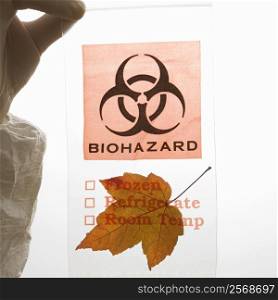 Hand wearing white rubber glove holding plastic biohazard bag containing orange Maple leaf.
