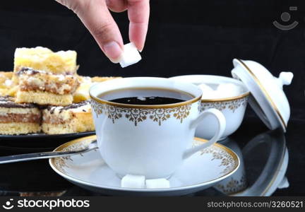 Hand, wich gives sugar lump to cup of coffee