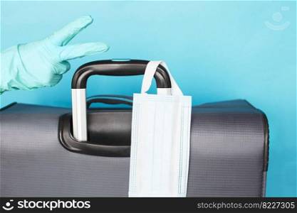 Hand with a luggage bag and medical mask isolated on a blue background. protection Coronavirus disease Covid-19 infection.. Hand with a luggage bag and medical mask isolated on a blue background. protection Coronavirus disease infection.