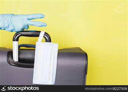 Hand with a luggage bag and medical mask isolated on a yellow background. protection Coronavirus disease Covid-19 infection.. Hand with a luggage bag and medical mask isolated on a yellow background. protection Coronavirus disease infection.