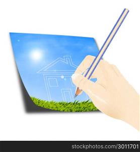 Hand with a pencil drawing a house of dream against blue sky and green grass.