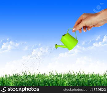 Hand with a small watering can watering green grass