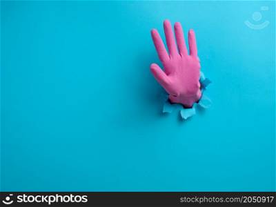 hand with an open palm sticks out of a torn hole in blue paper, gesturing to stop