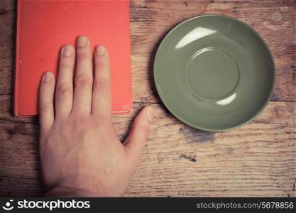 Hand with book and saucer at a table