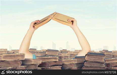 Hand with book reaching out from pile of old books. Book search