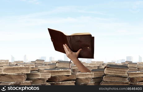 Hand with book reaching out from pile of old books. Book search